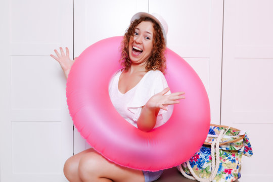 Woman sitting on luggage with inflatable round and ready for vacation trip. Preparing for the vacation concept