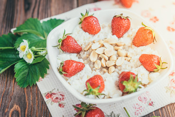 Oatmeal with cottage cheese, peanut and strawberries on wooden background. Summer healthy breakfast.