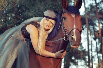 beautiful girl blond rider in hat in dress on horse walk in coniferous forest