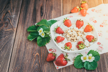 Oatmeal with cottage cheese, peanut and strawberries on wooden background. Summer healthy breakfast.