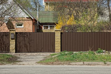 part of the brown fence and closed gate of iron on the street near the road