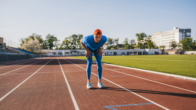 Athletic handsome male relaxing after intense workout and running on stadium. Athlete taking rest with hands resting on knees after a jogging and run standing on race track outdoor. People and sport