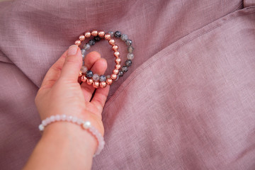 Rose gold stone bracelets in woman's hand, linen fabric background.  Female energy, fashion and beauty blogging concept