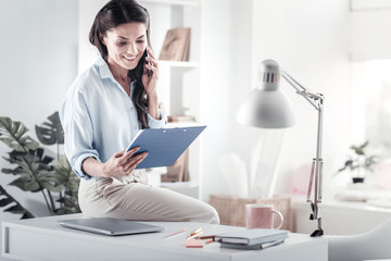 Office style. Attractive businesswoman keeping smile on her face while looking at documents
