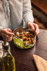 Woman's hands and a bowl of healthy green salad. Low key food photography, warm colors, toned image