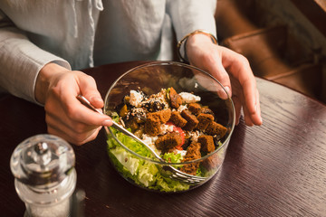 Woman's hands and a bowl of healthy green salad. Low key food photography, warm colors, toned image