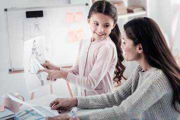 Modern model. Positive delighted child keeping smile on face while pointing at sketch