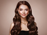 Brunette Girl with Long Healthy and Shiny Curly Hair. Care and Beauty. Beautiful Model Woman with Wavy Hairstyle. Make-Up and Jewelry