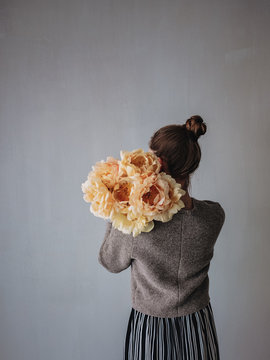 Rear view of woman holding peony flowers against gray wall