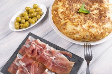 Omelette with olives and ham next to fork on wooden table. Typical spanish food.