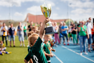 Young Boy Raising Golden Football Cup. Winning Youth Football Team Celebrating Success. Kids School Football Tournament Handing Out Prizes