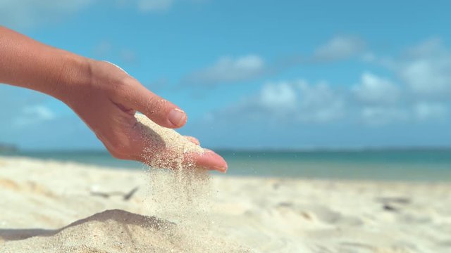 SLOW MOTION, CLOSE UP, LENS FLARE: Unrecognizable woman playing on paradise island beach lets the summer breeze blow away the sand from her gentle hand. Particles of sand flying out of girl's grasp.