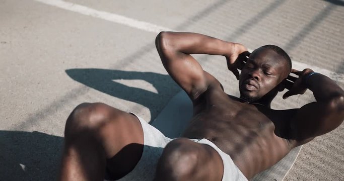 Athletic African American man is doing crunches on a grey mat on the street . Concept of health and fitness. 4k, real time shot