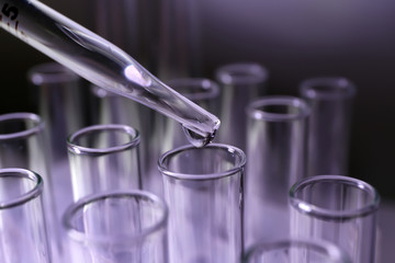 Pipette dripping sample into test tube on color background, closeup