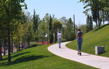 A man and a woman on scooters in the Park in the summer.