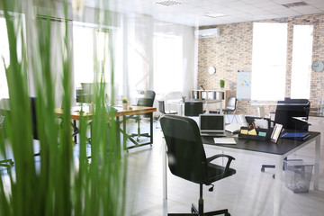 Office interior with tables and armchairs, view through glass. Workplace design