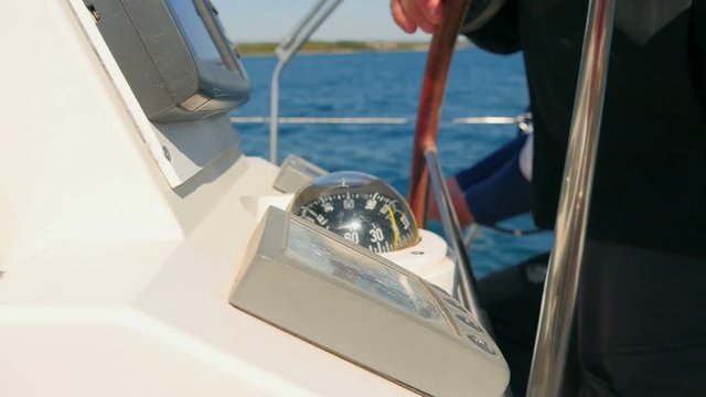 Sailors working on sailing boat man turning steering wheel and looking at compass. Another one in background winding ropes.
