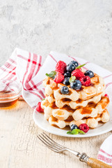 Belgian waffles with raspberries, blueberries and syrup, homemade healthy breakfast, light concrete background copy space