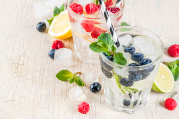 Various berry lemonade or mojito cocktails, fresh iced lemon lime raspberry blueberry infused water, summer healthy detox drinks light background copy space