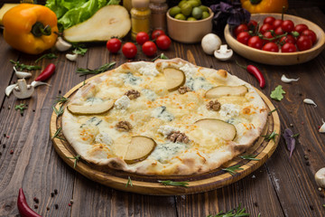 Italian pizza four cheese quattro fromaggi with pear and walnut on a rustic wooden board background
