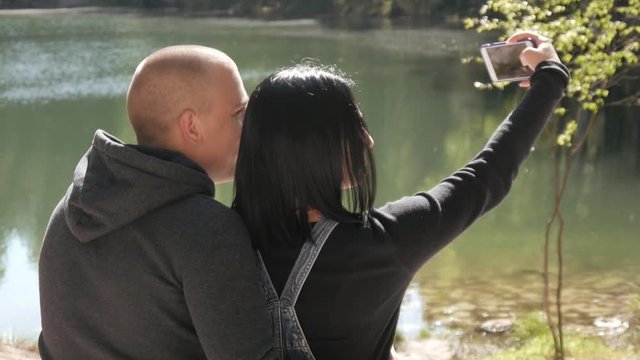 Young Guy and Girl sitting on Rock near the Lake, make Selfie Photo with iPhone