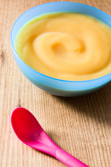 Baby food: Blue bowl of fruit puree on wooden table.