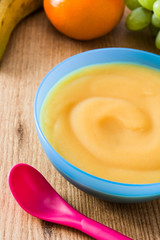 Baby food: Blue bowl of fruit puree on wooden table.