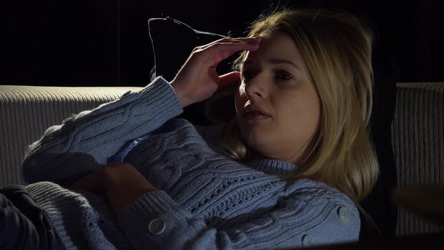 A young beautiful woman lies on a couch in a dark room and thinks about something sad - closeup