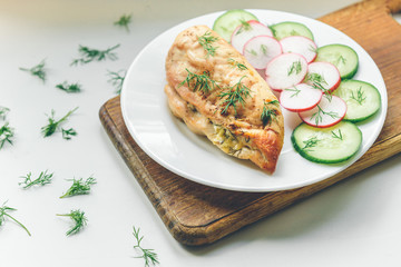 Baked chicken breast with cheese, cucumber and red radish on white plate. Healthy diet protein food.