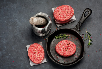 Raw burgers cutlets from beef meat with with pepper and rosemary in a frying pan on black background, top view