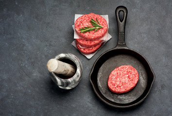 Raw burgers cutlets from a marble beef in a frying pan on a black background, top view