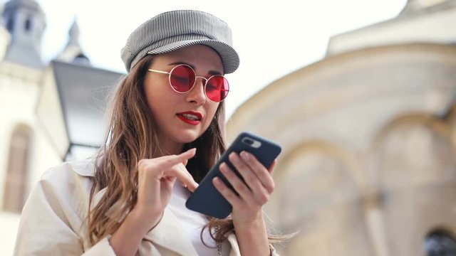 portrait of young brunette attractive woman using smart phone mobile outside checking notification with upset face disappointment serious business lady casual look red lips pretty female person device