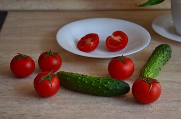 Red ripe tomatoes and green cucumbers lie on the kitchen table.