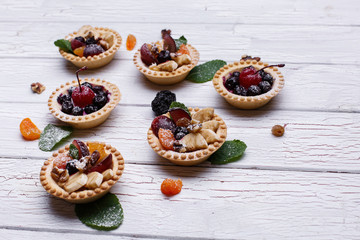 Delicious baked fruit baskets with berries, exotic fruits, greenery and nuts served on white wooden table