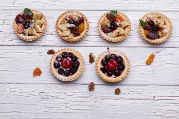 Delicious baked fruit baskets with berries, exotic fruits, greenery and nuts served on white wooden table