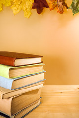 Stack of old books is lying on wooden table on light background with autumn maple leaves and copy space.