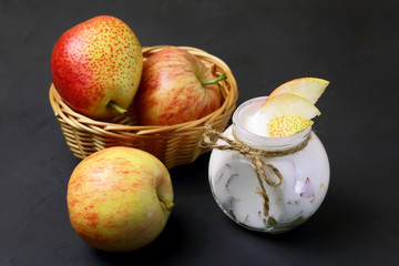 Food. Dessert of milk. Dairy product on a black background. Creamy yogurt in a glass jar with pieces of fresh juicy pears and red apples for a healthy diet.
