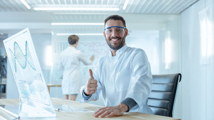 In the Futuristic Laboratory Male Scientists Showing  Thumb Signal. He is Working on the Transparent Display Computer. Screen Shows Interactive DNA Visualisation and Futuristic User Interface.