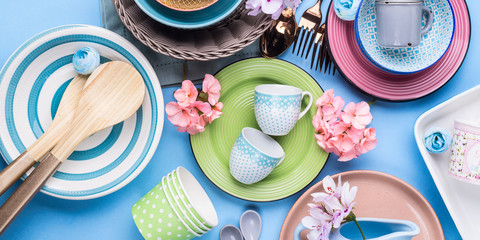 Tableware dish set on blue pastel background with flowers. Flat lay