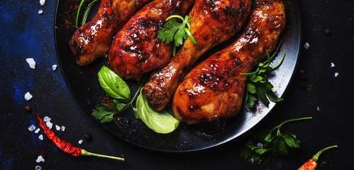 Baked chicken legs in spicy glaze with hiney sauce on the plate, black background, top view
