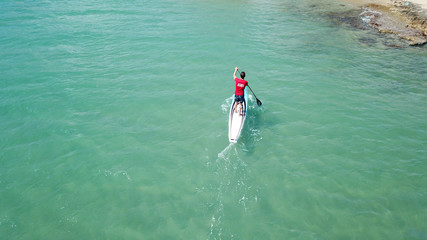 Aerial drone bird's eye view of 2 men exercising sport sup board in turquoise clear waters, Greece