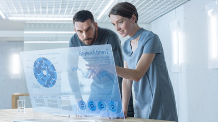 In the Near Future Male and Female Trade Agents Talk While Working on the Transparent Display Computer. Screen Shows Economical Graphs, Analysis of Trade, Futuristic User Interface.