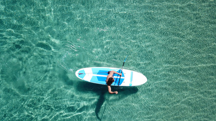 Aerial drone bird's eye view of a man exercising sup board in turquoise tropical clear waters at sunset