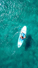 Aerial drone bird's eye view of a man exercising sup board in turquoise tropical clear waters