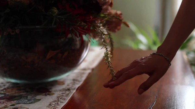 Woman's hand touches bouquet of dried flowers in vase on table.