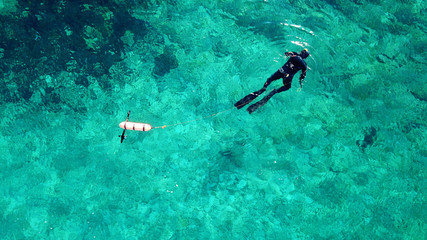 Aerial drone bird's eye view photo of scuba diver in tropical rocky sea with turquoise clear waters