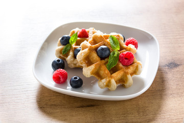 Traditional belgian waffles with blueberries and raspberries on wooden table