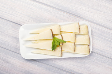 Cheese cut on plate next to fork on white and blue wooden table. Food