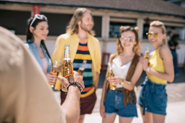 cropped shot of man holding beer bottle near friends drinking beer at beach bar