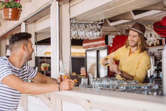 smiling bartender and client with beer bottle looking at each other in beach bar